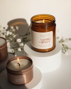 two candles sitting next to each other on top of a white surface with flowers in the background