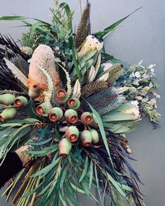 an arrangement of flowers and foliage on a wall in front of a gray wall with a person's hand holding it