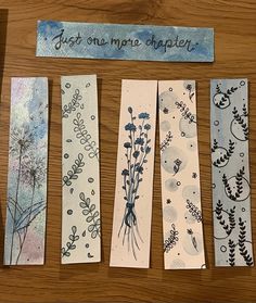 four bookmarks with different designs on them sitting on top of a wooden table next to a sign that says just one more chapter