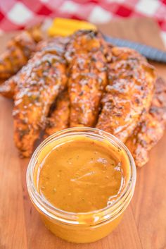 grilled chicken wings and sauce on a cutting board next to a jar of barbecue sauce