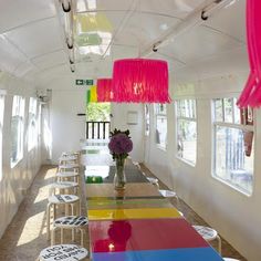 a long table with chairs and colorful lights hanging from it's ceiling in a brightly lit room