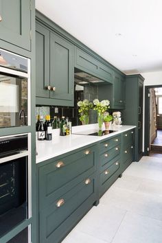 a kitchen with green cabinets and white counter tops is pictured in this image, there are flowers on the counter