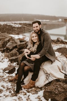 a man and woman are sitting on rocks in the snow with their arms around each other