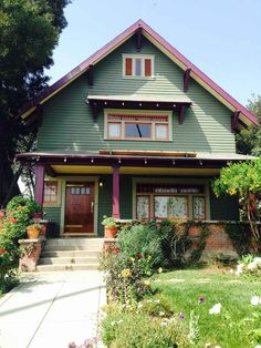 a green house with red trim on the front door and two story windows, surrounded by greenery