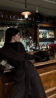 a woman sitting at a bar in front of a wooden cabinet with bottles on it