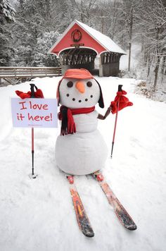 a snowman with skis holding a sign that says i love it here