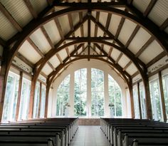 an empty church with rows of pews in front of large windows and wood beams