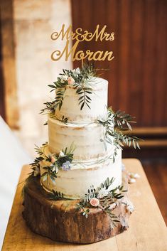 a white wedding cake with greenery and mr and mrs topper on wooden stand