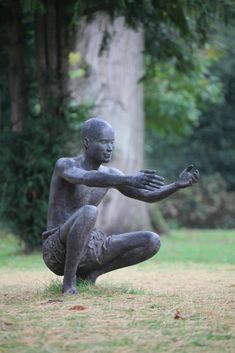 a statue of a man sitting on the ground in front of a tree and grass area