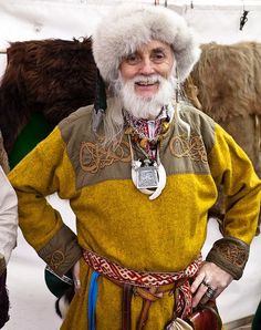 an old man with white hair and beard wearing a yellow outfit standing in front of some sheep