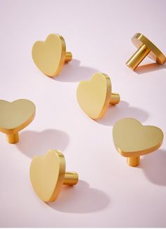 four gold heart shaped knobs on a pink background