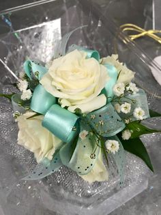 a white rose and blue ribbon corsage on an acrylic box with ribbons