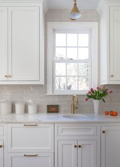 a kitchen with white cabinets and a gold faucet in the window sill