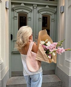 a blonde woman holding a bouquet of flowers in front of a building door with an entrance