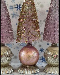 two pink and gold christmas trees are on top of silver vases in front of a wall with snowflakes