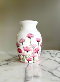 a white vase with pink flowers painted on the side sitting on a marble countertop