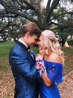 a man in a blue suit and tie standing next to a woman wearing a blue dress