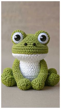 a crocheted frog sitting on the ground with big eyes and mouth wide open