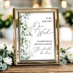 a wedding sign with flowers and greenery in front of it on a wooden table