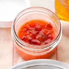 a jar filled with red sauce sitting on top of a table next to a plate