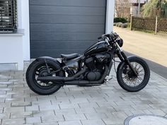 a black motorcycle parked in front of a garage door on a brick walkway next to a driveway