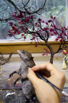 a person is painting a tree with red leaves on it in front of a window