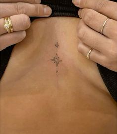 a woman is showing off her tattoo on the back of her stomach, with two gold rings around her neck