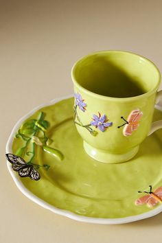 a green cup and saucer on a plate with butterflies painted on the rims