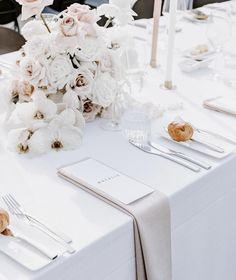 the table is set with white flowers and silverware