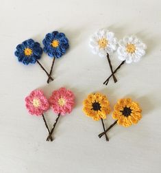 four crocheted flowers are arranged on a white surface