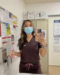 a woman in scrubs holding up a cell phone and wearing a surgical face mask