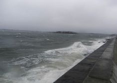 the ocean is choppy and stormy with waves crashing against the concrete wall, as people watch