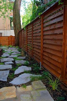 a stone path in front of a wooden fence next to a tree and grass area