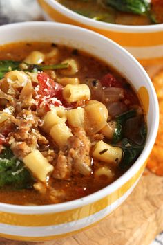 two bowls filled with pasta and spinach soup on top of a wooden cutting board