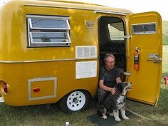 a man and his dog are sitting in the doorway of an old yellow camper