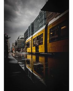 a yellow and white train traveling down tracks next to tall buildings on a rainy day