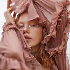 a woman in a pink dress with ruffles on her head and hands behind her head