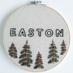 an embroidered hoop with the word easton written in black and surrounded by pine trees, on a white background