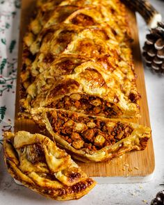 a wooden cutting board topped with sliced meat and cheese pastry next to pine cones on top of a table