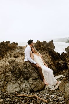 a man and woman are sitting on rocks by the ocean with their arms around each other