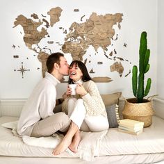 a man and woman sitting on top of a bed next to each other in front of a world map