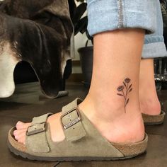 a woman's foot with a small flower tattoo on her left ankle and a dog in the background