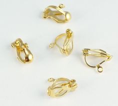 four pairs of gold plated ear clips on a white surface with clippings