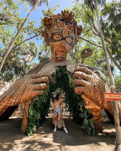 a woman standing in front of a large wooden sculpture with leaves on it's face