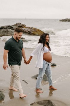 a pregnant couple walking on the beach holding hands