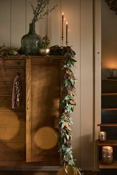 a wooden cabinet with candles and greenery on it in front of a set of stairs