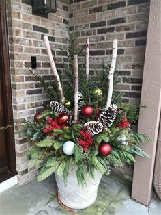 a potted plant with pine cones and ornaments on the front door sill for christmas