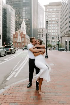 a man and woman are hugging in the middle of a city street with tall buildings behind them