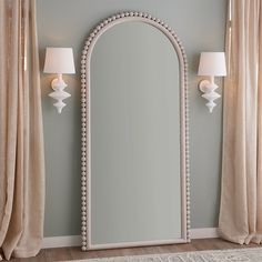 a large mirror sitting on top of a wooden floor next to two lamps and curtains