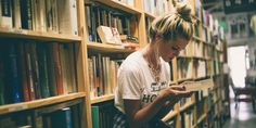 a woman sitting in front of a bookshelf reading a book